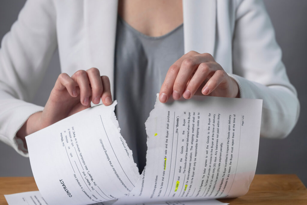 Torn contract in hands. Terminated agreement concept. Ripping paper document and breaching rules.