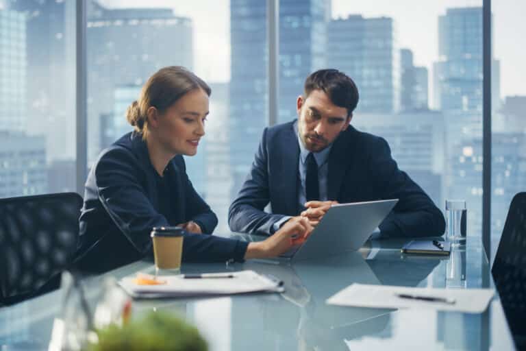 Successful Corporate CEO and Investment Manager Talking, Using Laptop Computer while Sitting in Meeting Room in Office. Two Successful Businesspeople Brainstorm on e-Commerce Marketing Project.